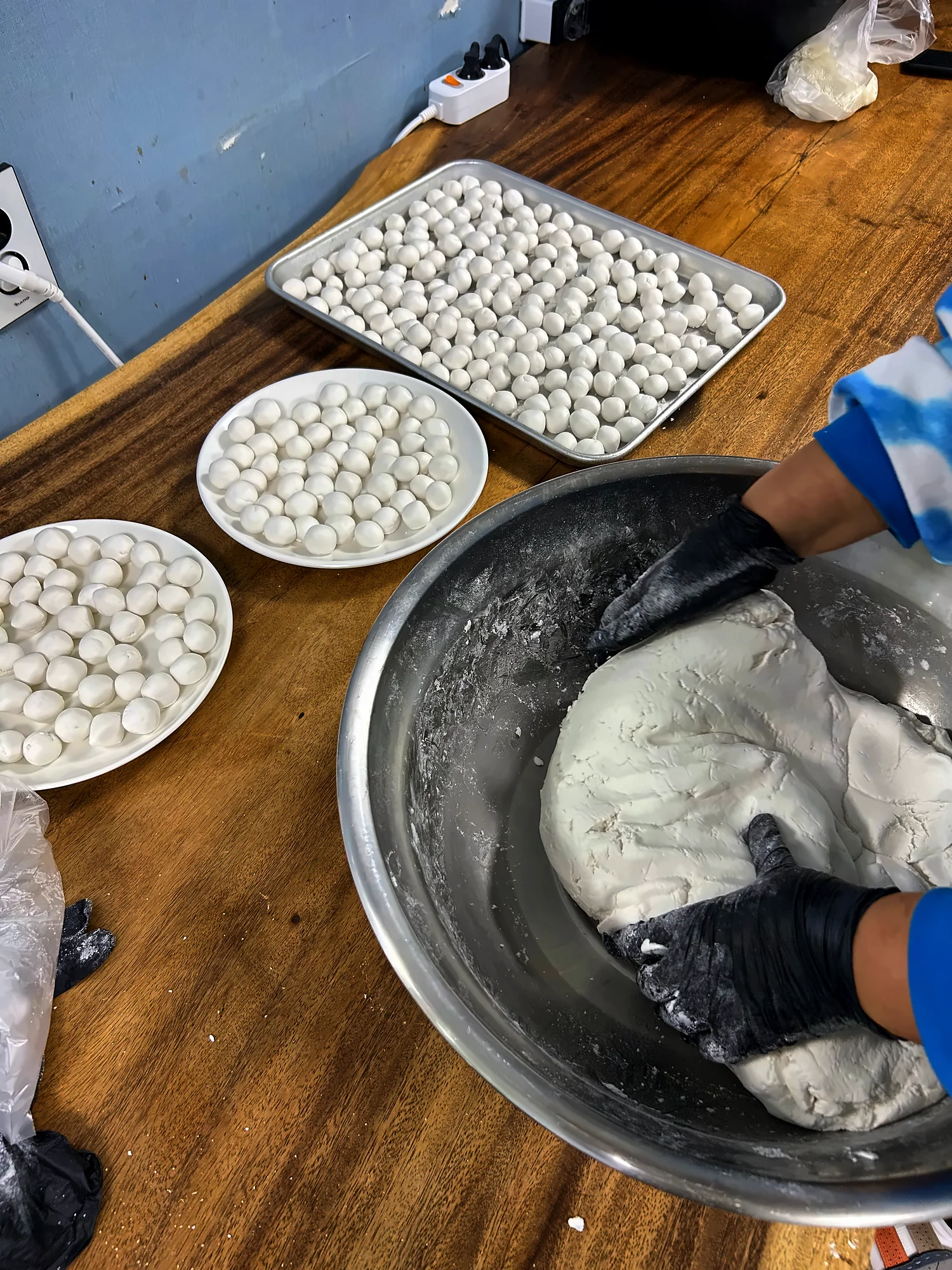 장갑 낀 손이 큰 그릇에서 흰 반죽을 치대고, 옆 쟁반에 동그랗게 빚은 새알심이 놓인 모습