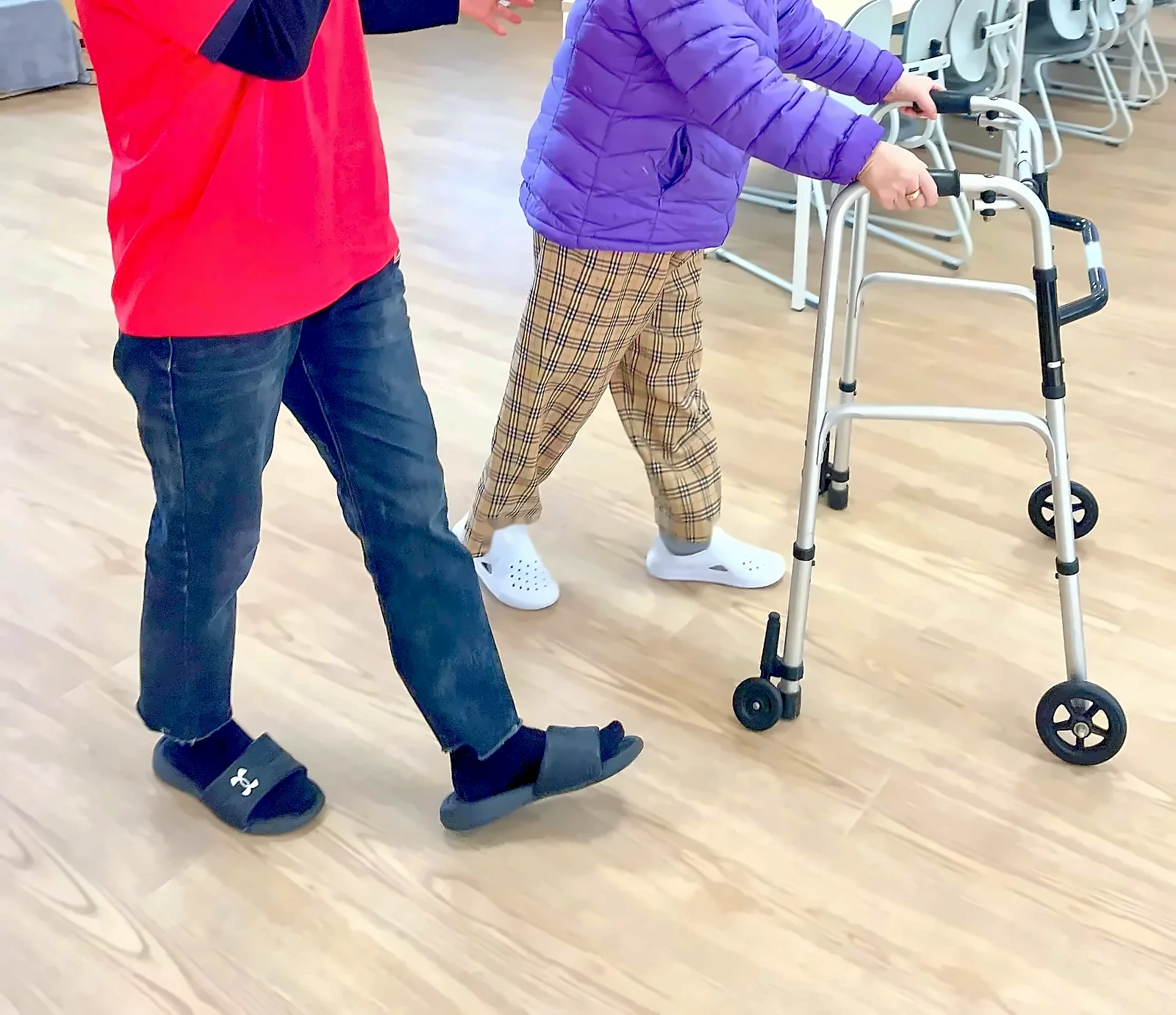 보행기를 밀며 걷는 어르신 곁에서 선생님이 함께 걷는 모습